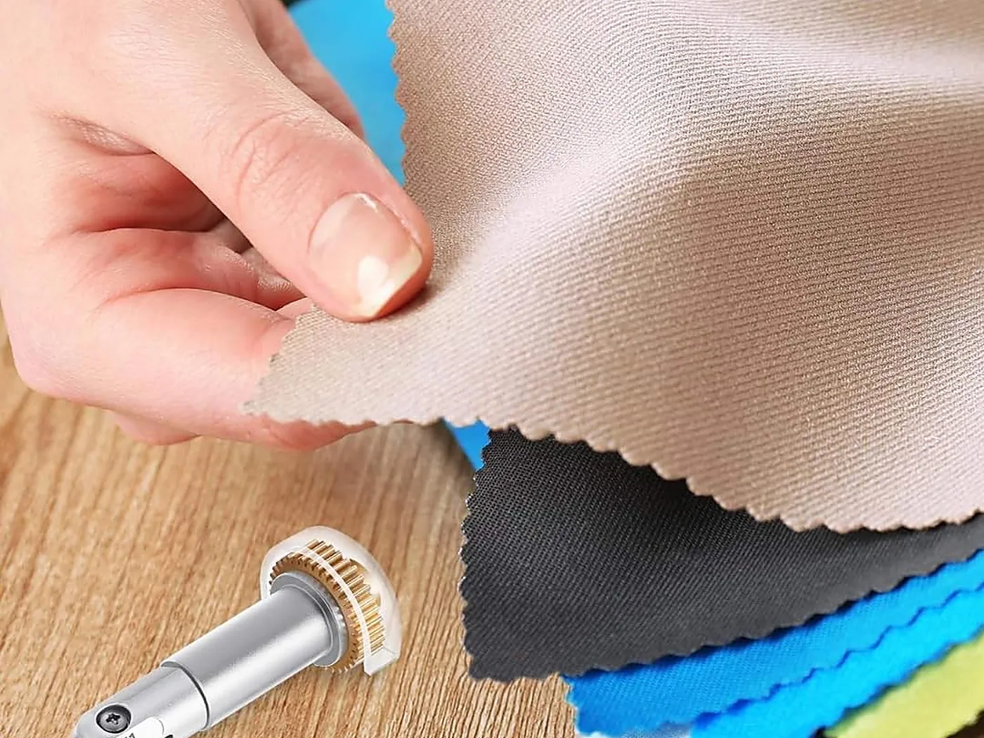 Une main soulève un tissu beige parmi une pile de textiles de couleurs différentes, à côté de la lame ondulée Wellkitch.
