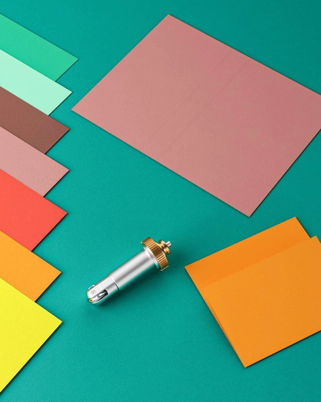 Papiers de couleur disposés en éventail autour d’une feuille rainée et de l’outil de rainage Wellkitch.
